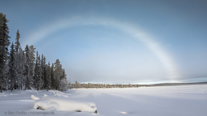 Die tiefstehende Sonne erzeugt über dem leichten Nebel über dem See Pallasjärvi eionen Nebelbogen.